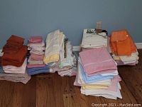Wide view of four large stacks of folded towels in varying colors including burnt orange, pink, white, blue, yellow, beige, and purple placed on wooden floor against blue wall.