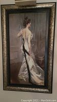 Full view of framed decorative print showing woman in satin gown with clip-on lamp attached at top.
