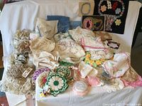 Full display of over 120 textile items including doilies, trims, embroidered pieces, samplers, arranged on white backdrop
