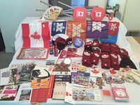 Wide view showing the collection spread on a table including Canada flags, Expo 67 memorabilia, Olympic souvenirs, pins, gloves, hats, Coca-Cola bottles, and brochures.