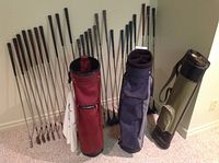 Display of three golf bags (green, red, blue) with multiple golf clubs lined up behind them showing the mix of irons and woods.