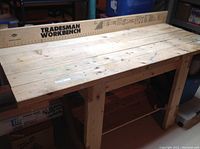 Full view of wooden workbench showing top surface, wooden planks, and backboard with 'Tradesman Workbench' branding.