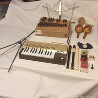 Full view of entire lot including keyboard, xylophone, recorders, maracas, music stand, accessories seen arranged on white fabric.
