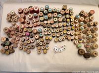 Top-down photo showing over 170 wood thread spools arranged with labels visible. Assorted colors and brands.