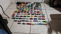 Full view of over 100 various die cast toy vehicles lined up on floor