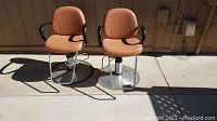 Pair of two tan upholstered Belvedere barber chairs side by side on a patio, showing general condition and style.