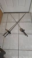 Full view of two vintage fencing swords with tapered blades and round guards laid down on tile floor.
