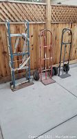 Photo showing all three hand trucks side by side against a wooden fence on concrete floor.