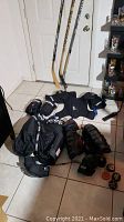 Full view of hockey gear including sticks, pads, gloves, shorts, pucks, and ball on tiled floor indoors
