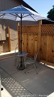 Full view of outdoor bistro set with umbrella open for shade on concrete patio next to wooden fence.