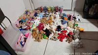 Photo showing the collection of Barbies, TY Beanie Babies, and Troll dolls arranged on the floor with visible ear tags on the TY Beanie Babies and a bin of Barbie clothes.