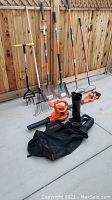 Wide view of the yard tools showing rakes, shovels, hand tiller, and two Black & Decker blowers with black collection bag