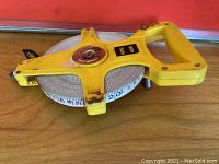 Yellow 30m measuring tape reel showing front side with handle and tape extended slightly showing metric measurements.