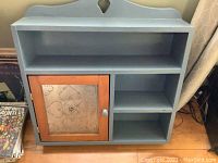 Front view of the blue painted wooden shelf cabinet with a tin and wood door on the left and open shelving on the right.