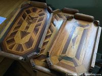 Three nesting hardwood trays stacked showing the intricate geometric indigenous wood inlay design and rounded wooden handles.