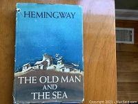 Front of dust jacket for The Old Man and the Sea by Ernest Hemingway, color illustration of village, some wear and tear