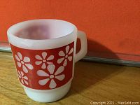 Side view of red daisy floral pattern on the vintage Fire King opaque milk glass mug with D-shaped handle