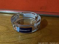 Clear glass ashtray with 'EXPORT A' label and vintage woman image sitting on wooden surface, showing the top and side view of the ashtray.