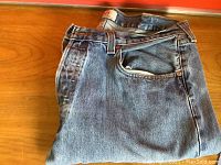 Folded vintage Levi's blue denim jeans showing front pocket and belt loops on wooden surface