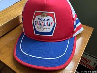 Front view of vintage Molson Canadian trucker hat showing red crown and blue bill with white piping.