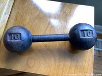 Full view of the vintage cast iron barbell dumbbell on wooden table, showing both weighted ends embossed with '10'.