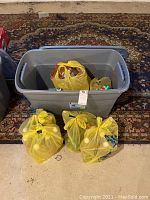 Gray plastic lidded storage bin with several yellow plastic bags inside and outside.