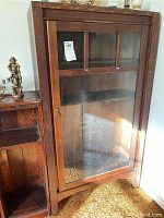 Front view of the wood display cabinet showing the single glass door with wooden grid and brass handle