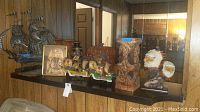Photo showing model ships, wooden carvings, eagle figurine, and framed Egyptian wall art on a shelf