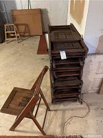 Stack of 19 wooden folding chairs with visible scratches and wear, showing the folding mechanism and backside of chairs.