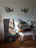 Photo showing folding table, peacock wall art, framed art, candle holders, candle lanterns, planter with faux plant, and a banker lamp grouped on and around the table.