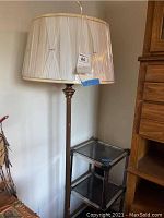 Floor lamp with pleated cream fabric shade and lower shelving unit with glass shelves and chrome frame