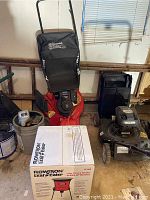 Full lot image showing orange Rally lawn mower without wheels, Flowtron Leaf Eater box, and gray plastic gas can in a garage setting.