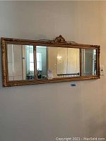 Full frontal view of the rectangular framed mirror hung on a wall showing reflective sections and ornate gold frame.