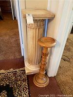 Photo showing two decorative pedestals side by side: a tall classical fluted column pedestal and a shorter carved wooden pedestal.
