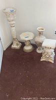 Photo showing all four items: a tall planter on stand, two pedestals, and a vase, all white with ornate carvings