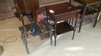 Two side tables positioned together. One is black marble top with beige veining and brass legs, the other is a rectangular wooden table with a drawer and lower shelf.