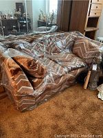 Full view of the Sears sofa covered in plastic. Shows the geometric patterned upholstery in browns and tans.