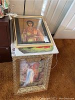 Stack of framed artwork, top piece is a classical portrait of a religious figure in robes.