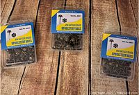 Three boxes of antique brass upholstery nails arranged on wooden surface.