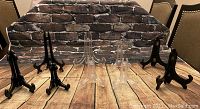 Black wooden easels and clear plastic easels arranged on a table with a brick backdrop.