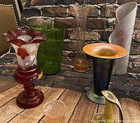 Full view of all vases and mini pitcher showing variety in color, material, and shape against brick background