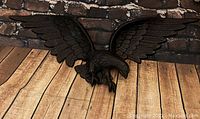 Cast iron American eagle wall sculpture with outstretched wings and detailed feathering on wood floor against a brick wall.