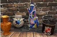 Overview of the four ceramic and stoneware items: one brown cheese crock, abstract figura, orange vase, and floral vase