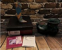 Ceramic Paisley West boot figurine on original box with certificate and bracelet charms on wooden floor against brick background