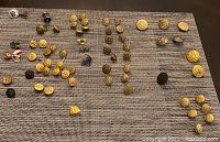 Overview of assorted vintage buttons, pins and thimbles laid out on a textured mat showing groups of various military-style buttons and pins.