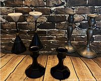 Set of five candle holders including two white marble topped black base holders, two tall silver holders, and two short cobalt blue holders shown on wooden surface with brick background