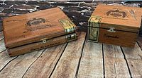 Two wooden vintage Arturo Fuente cigar boxes placed on a wood surface, showing the exterior designs, labels and gold seals on each box.