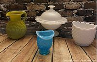 Photo showing four hobnail glassware items: green pitcher, white covered bowl, blue vase, white serving dish