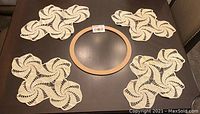 Crochet cream oval tablecloth and four matching swirling dollies laid out on dark wooden table with a wooden embroidery hoop in center for scale.