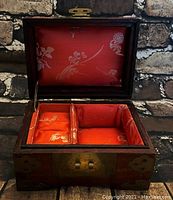 Open view of the vintage wooden jewelry box showing the red fabric interior with floral patterns and divided compartments, including cushioned ring holders.